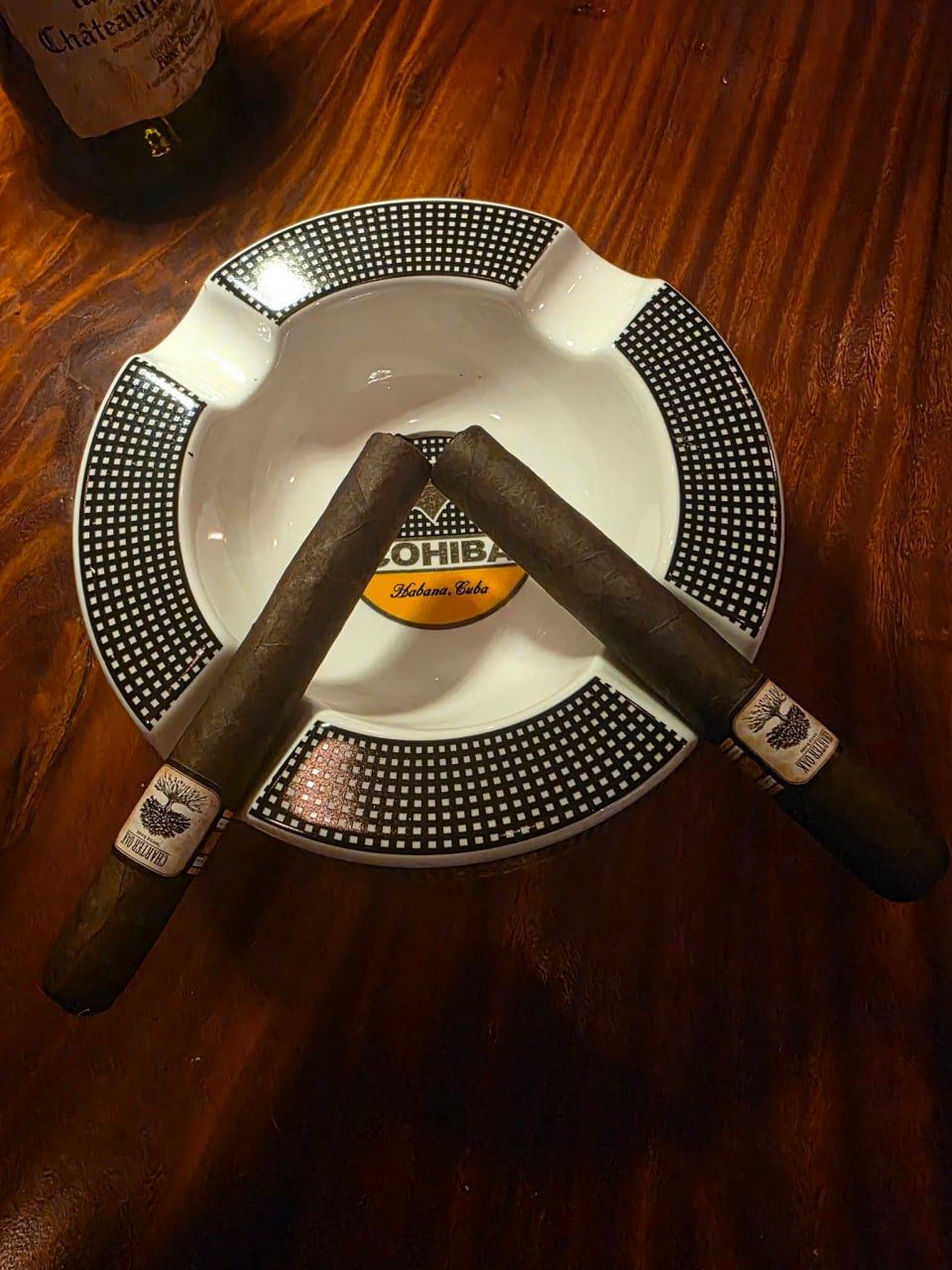 Two cigars resting crossed on a Cohiba ashtray on a polished wooden table