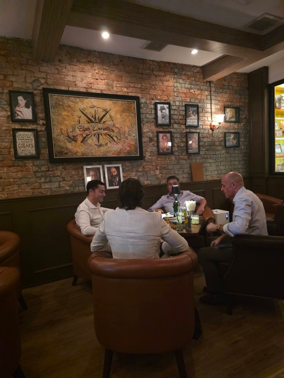 Guests seated in leather armchairs around a table beneath the framed Cigar Connection artwork