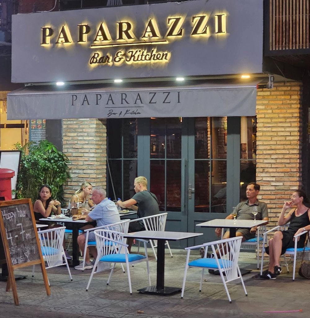 The Paparazzi Bar & Kitchen frontage on Preah Sisowath Quay at night — guests enter here and take the stairs to Cigar Connection